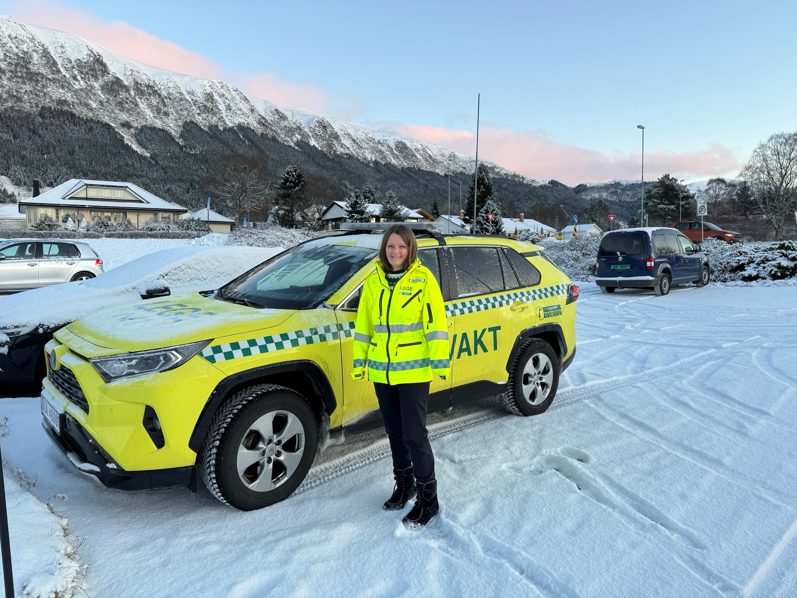 En person i uniform som står ved siden av en gul bil merket Legevakt i snøen