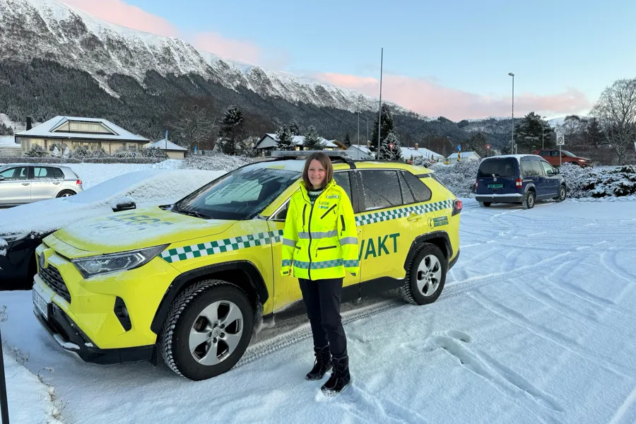 En person i uniform som står ved siden av en gul bil merket Legevakt i snøen