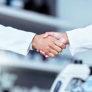 Bilde av to personer som tar hverandre i hendende, på bildet har de på seg hvite frakker og vi ser kun hendene