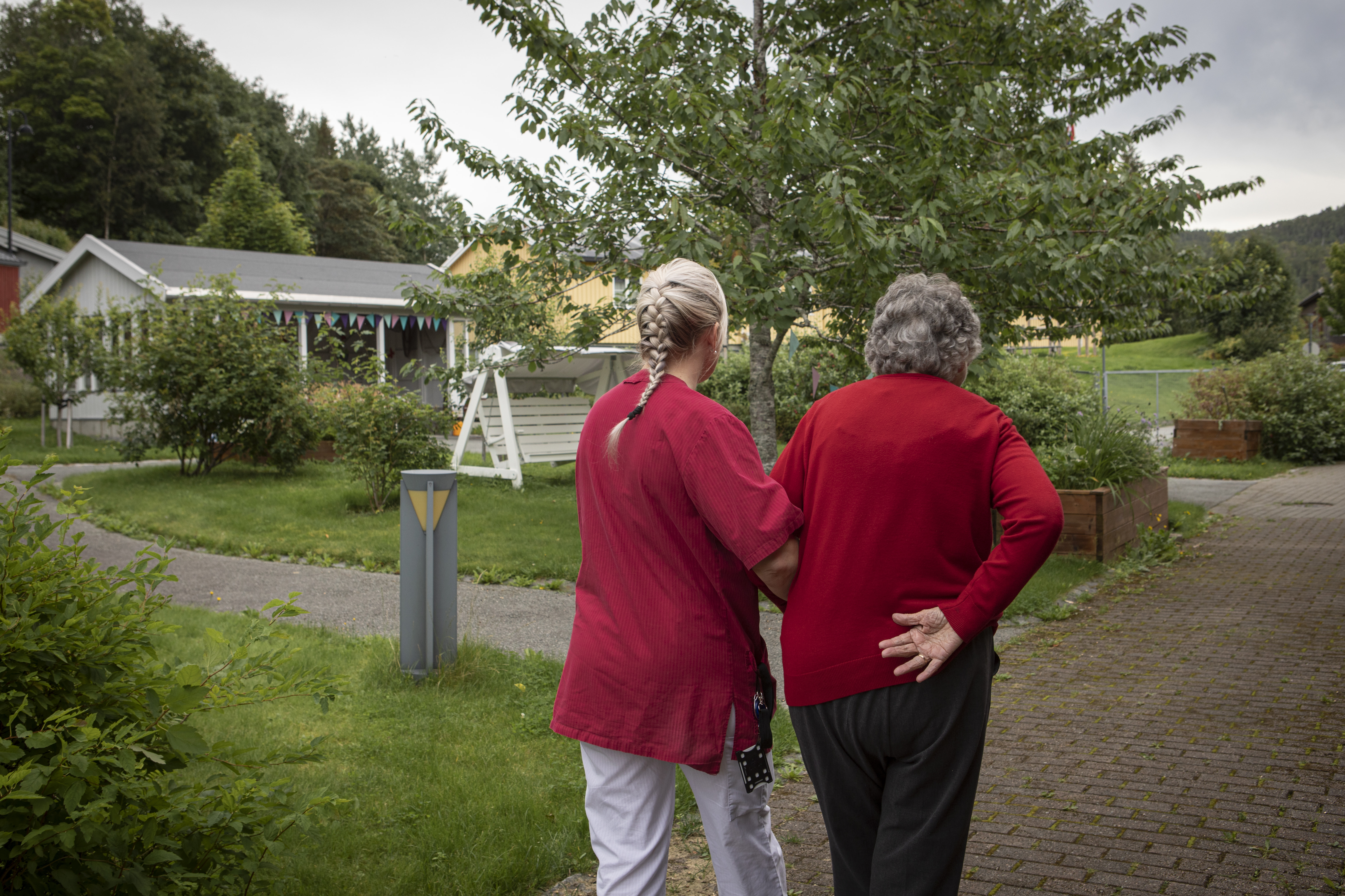 En eldre person og helsearbeider går tur i hagen