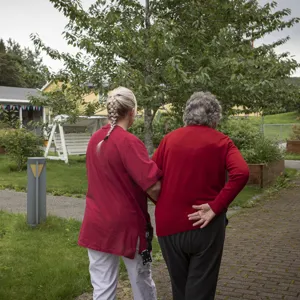En eldre person og helsearbeider går tur i hagen