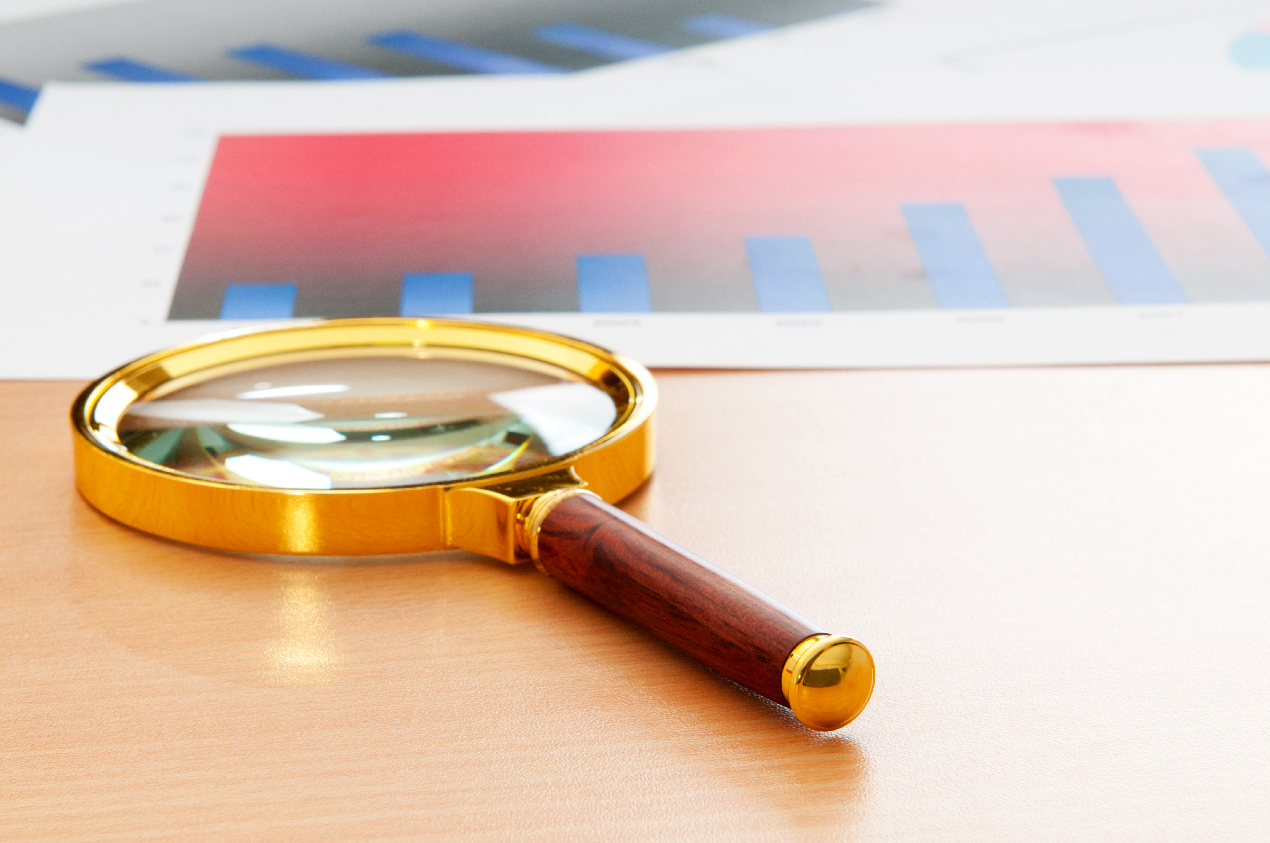 Forstørrelsesglass på et bord i varme fargetoner. Forstørrelsesglasset brukes som et symbol på å undersøke noe nærmere.