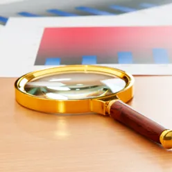 Forstørrelsesglass på et bord i varme fargetoner. Forstørrelsesglasset brukes som et symbol på å undersøke noe nærmere.