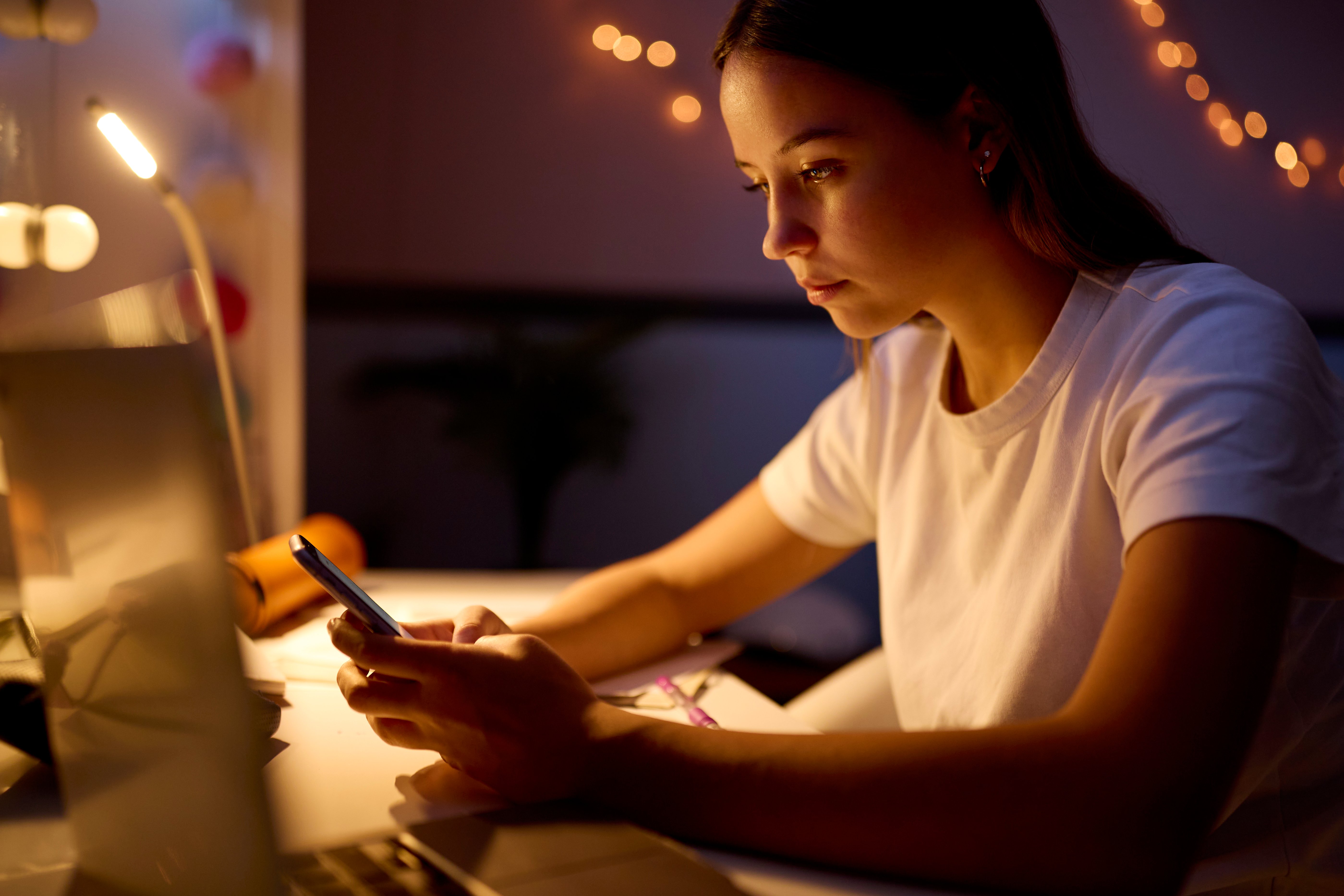 Ung kvinne sitter ved med skrivebord med mobiltelefon