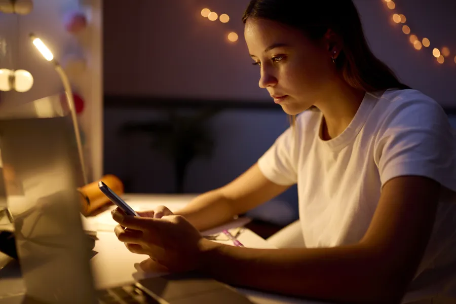 Ung kvinne sitter ved med skrivebord med mobiltelefon