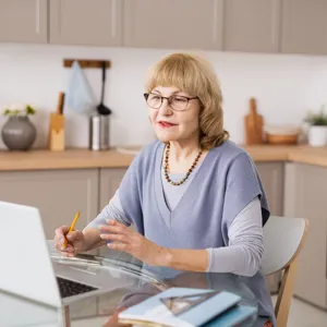 Dame med briller i 60-årene sitter ved kjøkkenbordet og har et møte på en bærbar datamaskin