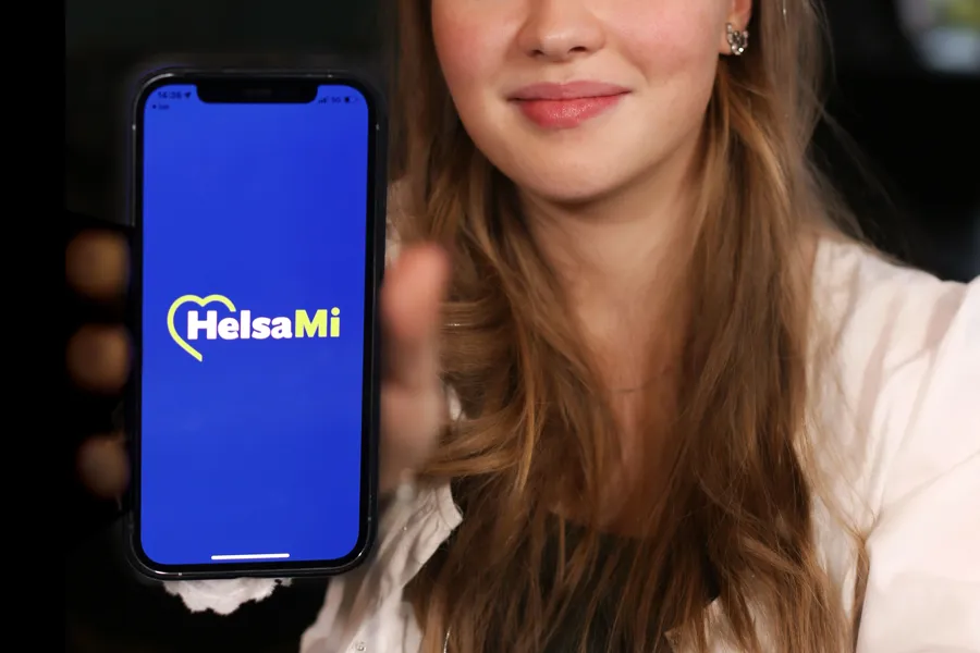 En kvinne som holder en telefon som viser bilde av HelsaMi-appen