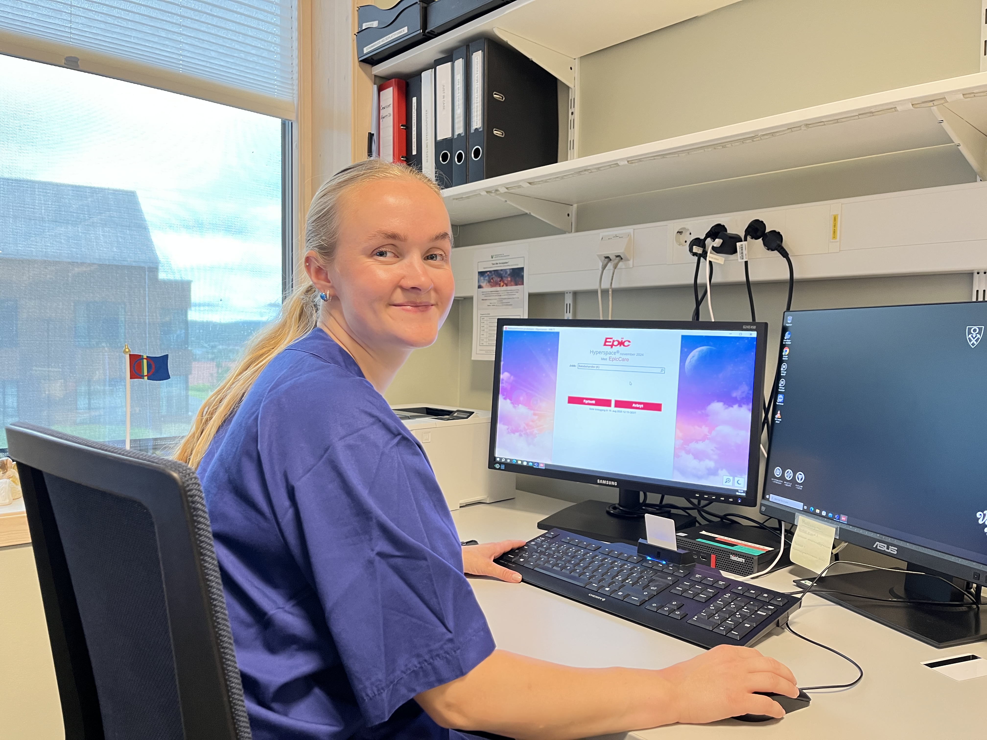 En dame i helsevesenet sitter ved et skrivebord med en datamaskin foran seg