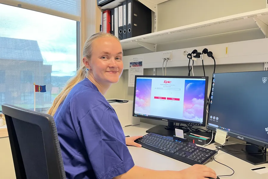 En dame i helsevesenet sitter ved et skrivebord med en datamaskin foran seg