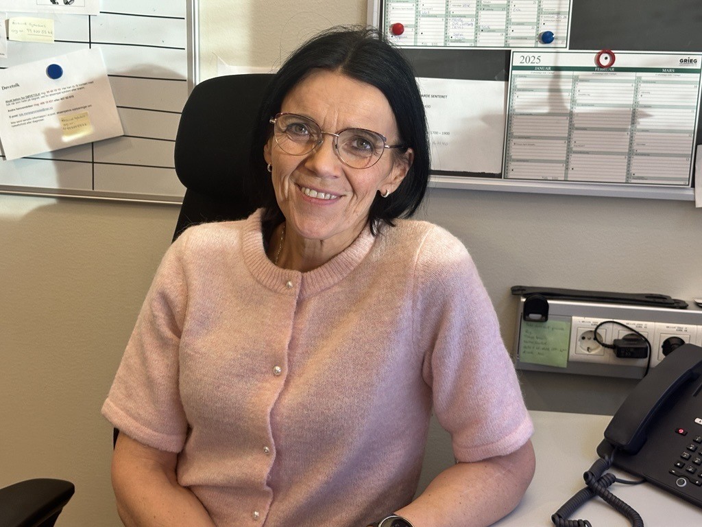 Marit Oline Molnes, medisinsk sekretær ved kreftavdelingen på Ålesund Sykehus, sitter ved skrivebordet og smiler mot kamera.