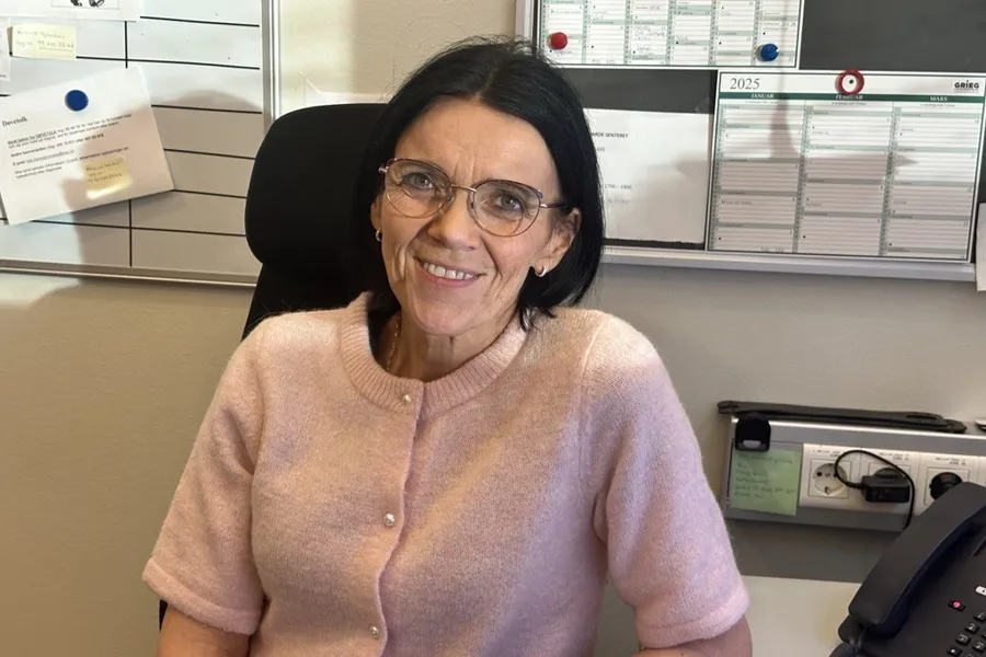 Marit Oline Molnes, medisinsk sekretær ved kreftavdelingen på Ålesund Sykehus, sitter ved skrivebordet og smiler mot kamera.