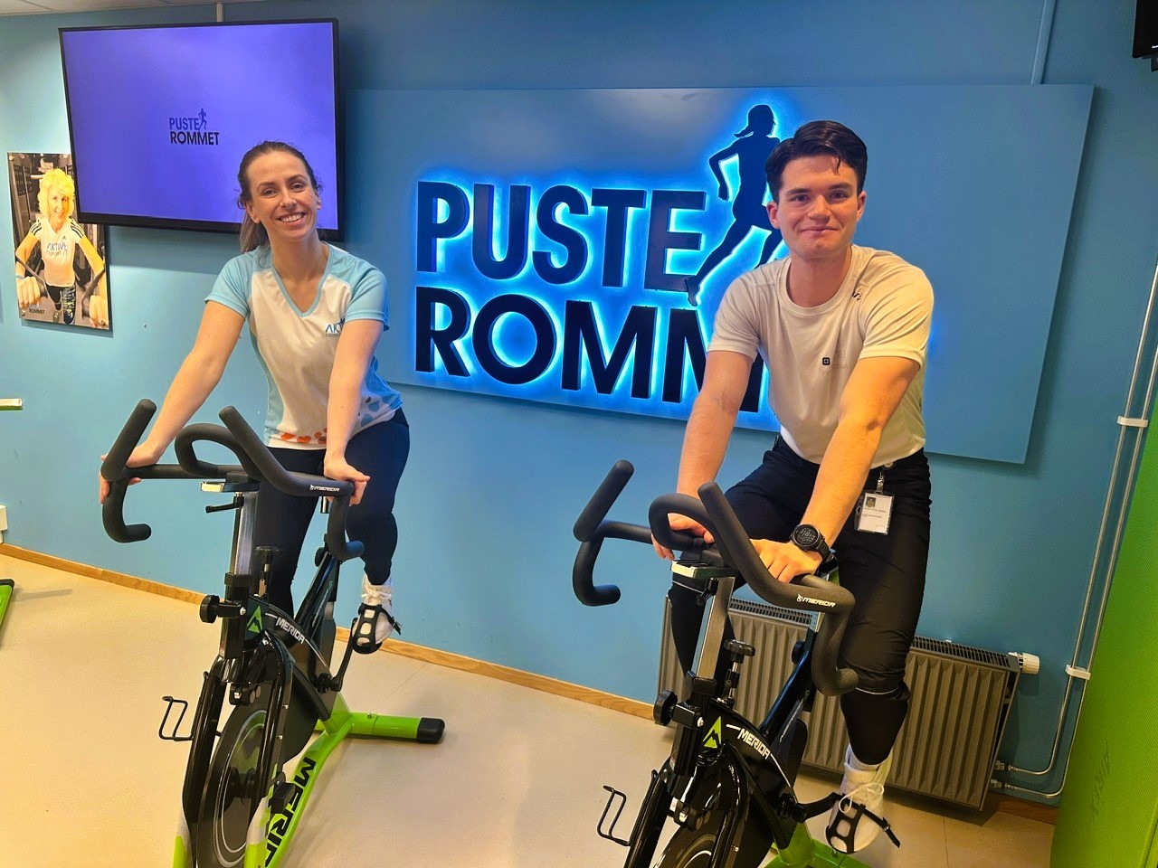 Fysioterapeut Sofie Hammernes Strømme og NTNU-student Joachim Sandor Knudsen sitter på spinningsykler på Pusterommet i Ålesund.